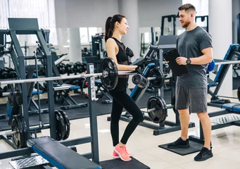 Fotobehang Personal trainer and client looking at his progress at the gym. Athletic man and woman wearing sportswear. © Vadim