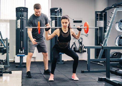 Young beautiful woman doing exercises with personal trainer. Beautiful girl squats under the supervision of the coach.