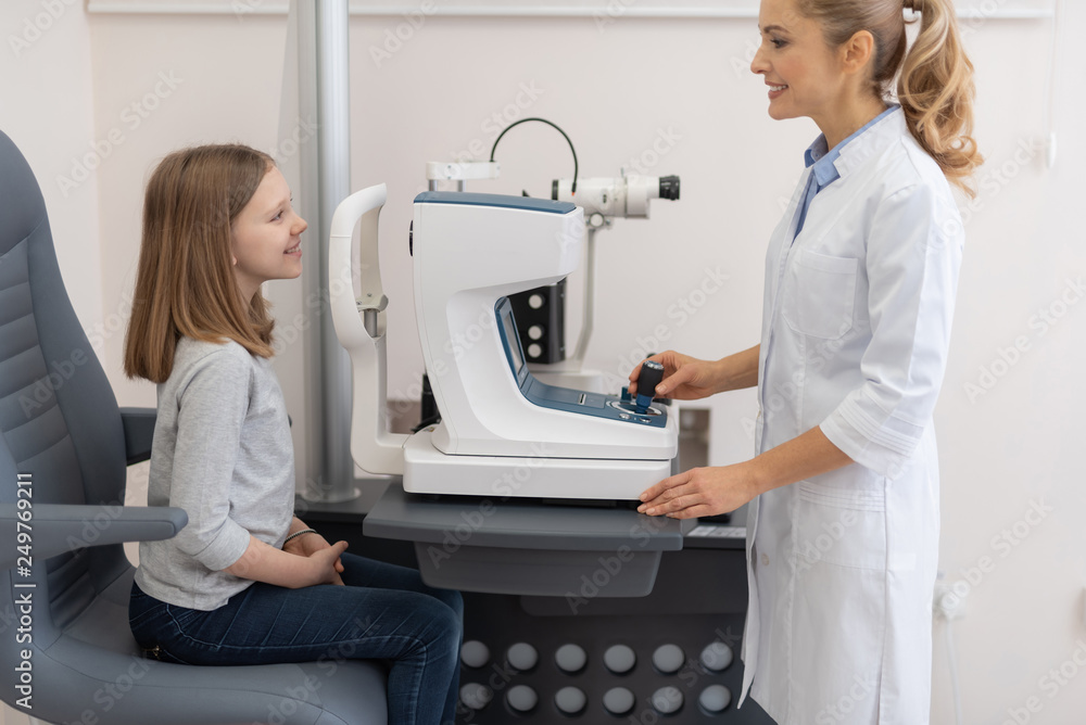 Poster female optometrist checking vision of little girl with autorefractor