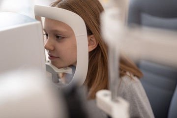 Cute little girl having eye examination at modern clinic