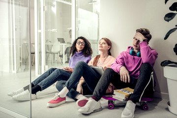 Blonde student sitting near his friends feeling tired and bored