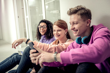 Cheerful handsome student with earphones on neck using his phone