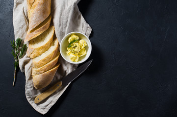 Sliced French baguette, butter and a sprig of rosemary. Black background, top view, close up, space...