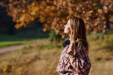 Beautiful European woman is standing in the wonderful autumn park. She is enjoying the fresh air and view.