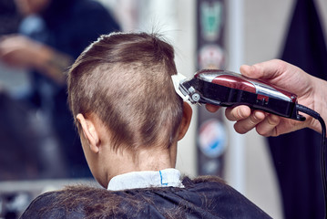 Hairdresser making a haircut to a boy with clipper. Back view.
