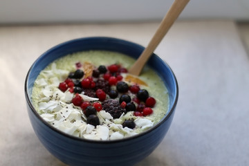 Fruit and vegetable smoothie (spinach, apple, banana, orange) with wild berries, chia seeds and coconut flake topping. Selective focus.