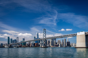 Bright blue skies with wispy clouds over the San Francisco skyline and the bay bridge crossing in...