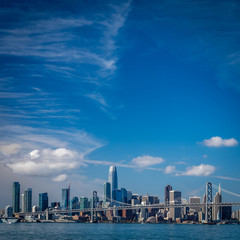 Mostly blue skies fill the picture of the San Francisco skyline and the bay bridge crossing in...