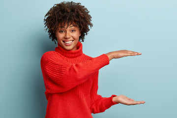 Indoor shot of happy woman with dark skin, Afro hairstyle, shapes height of object, has appealing...