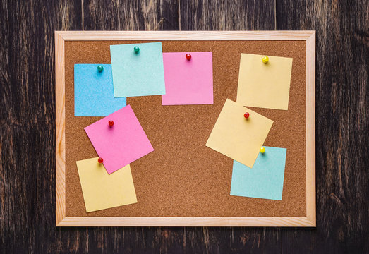 corkboard with pinned multicolored stickers on dark  background