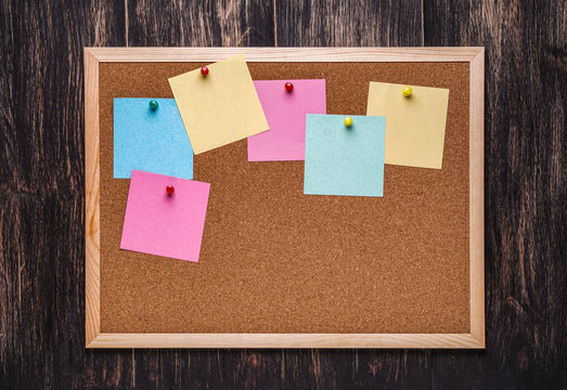 corkboard with pinned multicolored stickers on dark  background