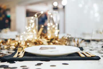 Dinner tableis decorated in black and gold. Garland in a glass flask. Golden fork and knife