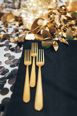 Dinner tableis decorated in black and gold. Garland in a glass flask. Golden fork and knife