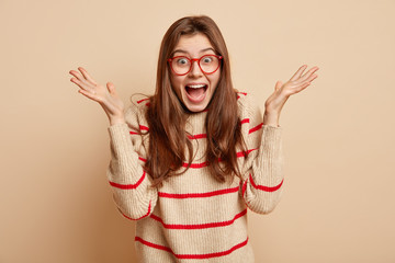 Euphoric pleased woman in high spirit, spreads palms, exlaims with joy, wears spectacles for vision...