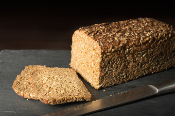 Sliced, fresh loaf of german bread with knife on slate board and timber background
