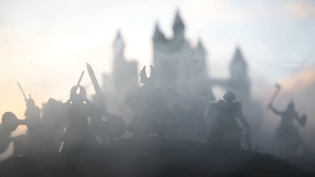 Medieval battle scene with cavalry and infantry. Silhouettes of figures as separate objects, fight between warriors on sunset foggy background. Selective focus