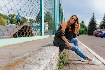 Fashion portrait of trendy young woman wearing sunglasses, jeans with halls and bomber jacket in...