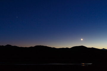 Moon, Venus, and Saturn in a deep blue twilight sky above a mountain silhouette