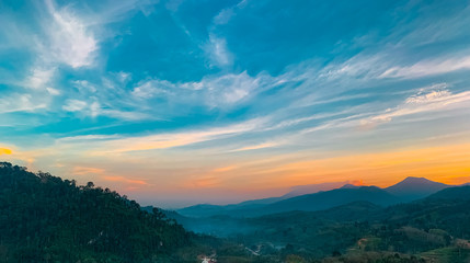 Fototapeta na wymiar Beautiful nature landscape of mountain range with sunset sky and clouds. Rural village in mountain valley in Thailand. Scenery of mountain layer at dusk. Tropical forest. Natural background.