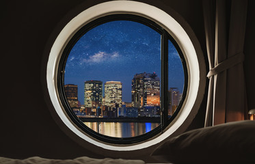 Fototapeta na wymiar Round window frame in bedroom at night with city view