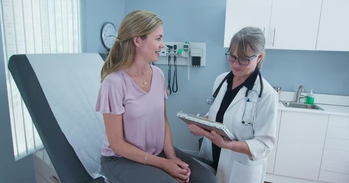 Two shot of woman talking to her primary care doctor in exam room. Middle aged patient having appointment with female senior physician. Slow motion 4k