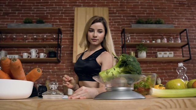 Cute young woman taking broccoli and putting on the scale to weighing it during cooking.