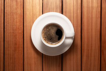Top view photo of a coffee cup and saucer over a wood table background
