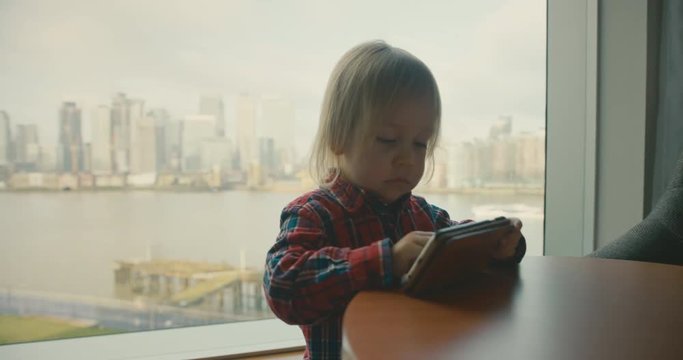 Little toddler playing game on smartphone by window in city apartment
