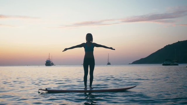 Young woman doing yoga on sup board with paddle at sunset. Concept of harmony with the nature, free and healthy living, freelance, remote business.