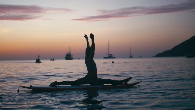 Young woman doing yoga on sup board with paddle at sunset. Concept of harmony with the nature, free and healthy living, freelance, remote business.