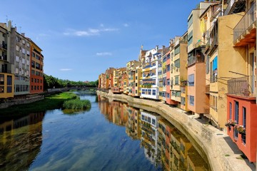 Colorful yellow and orange houses and Eiffel Bridge, Old fish stalls, reflected in water river Onyar, in Girona, Catalonia, Spain. Church of Sant Feliu at background.
