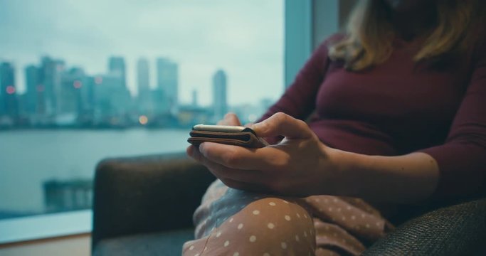 Young woman using smartphone by window in city apartment