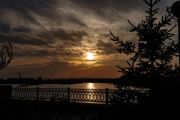 contour image of the embankment of the river at sunset under a golden sky and clouds, railings and...