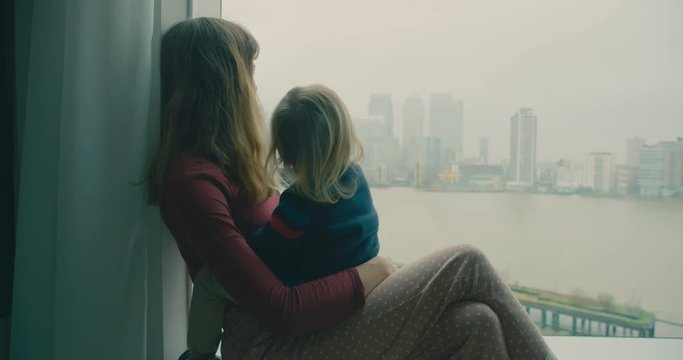 Mother and toddler are sitting by the window in a city apartment