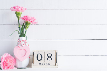 Womans day concept. Pink  carnation flower in vase and red heart with March 8 text on wooden block calendar on white wooden background.