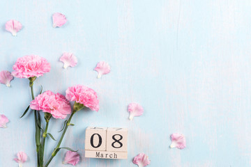 Womans day concept. Pink carnation flower with March 8 text on wooden block calendar on blue pastel wooden background.
