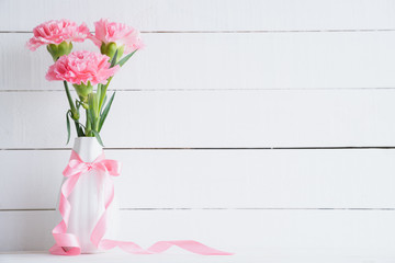 Valentines day and love concept. Pink carnation flower in vase with Wooden letters forming word LOVE written on white background.
