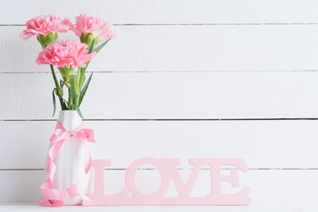 Valentines day and love concept. Pink carnation flower in vase with Wooden letters forming word LOVE written on white background.