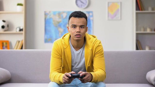 Addicted African-American teenager playing computer game showing no emotions