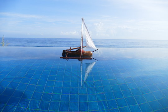 Photo picture of an amazing wooden small sailboat against the backdrop of amazing blue water, palm trees and the sea, enchanting with its naturalness