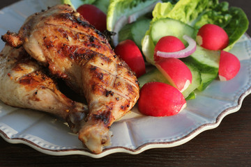 Grilled chicken quarters with salad for garnish on dark background.