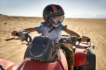 Kid in helmet and protect mask riding quad bike