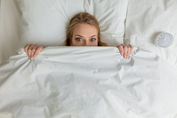 pleasant blonde girl hiding under the blanket and looking at the camera, fobia, emotion, feeling. top view photo.