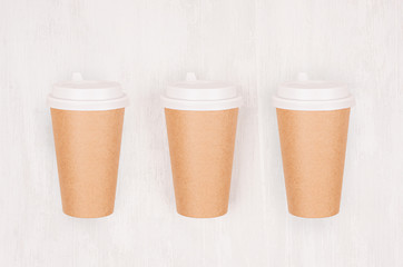 Set of three coffee kraft paper cups with cap on light wood board, top view. Mockup for branding...