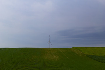 Fototapeta na wymiar Wind turbine on green field in stormy weather.