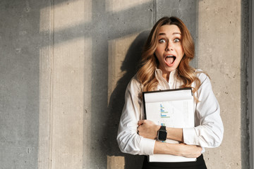 Beautiful young business woman dressed in formal clothes shirt indoors holding documents.
