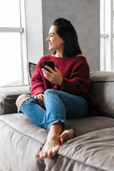 Beautiful woman indoors in home on sofa using mobile phone.