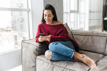 Beautiful woman indoors in home on sofa using mobile phone.