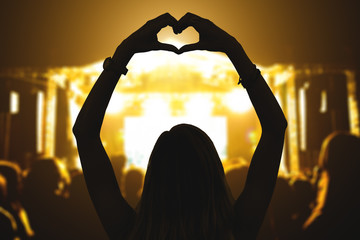 Girl with heart-shape symbol enjoying her favorite group on the concert.