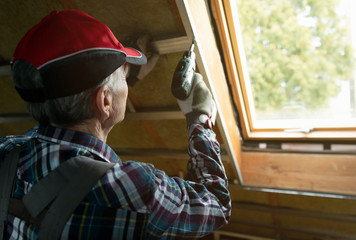 Attic insulation and renovation. Man fixing metal frame using an electric screwdriver on ceiling...